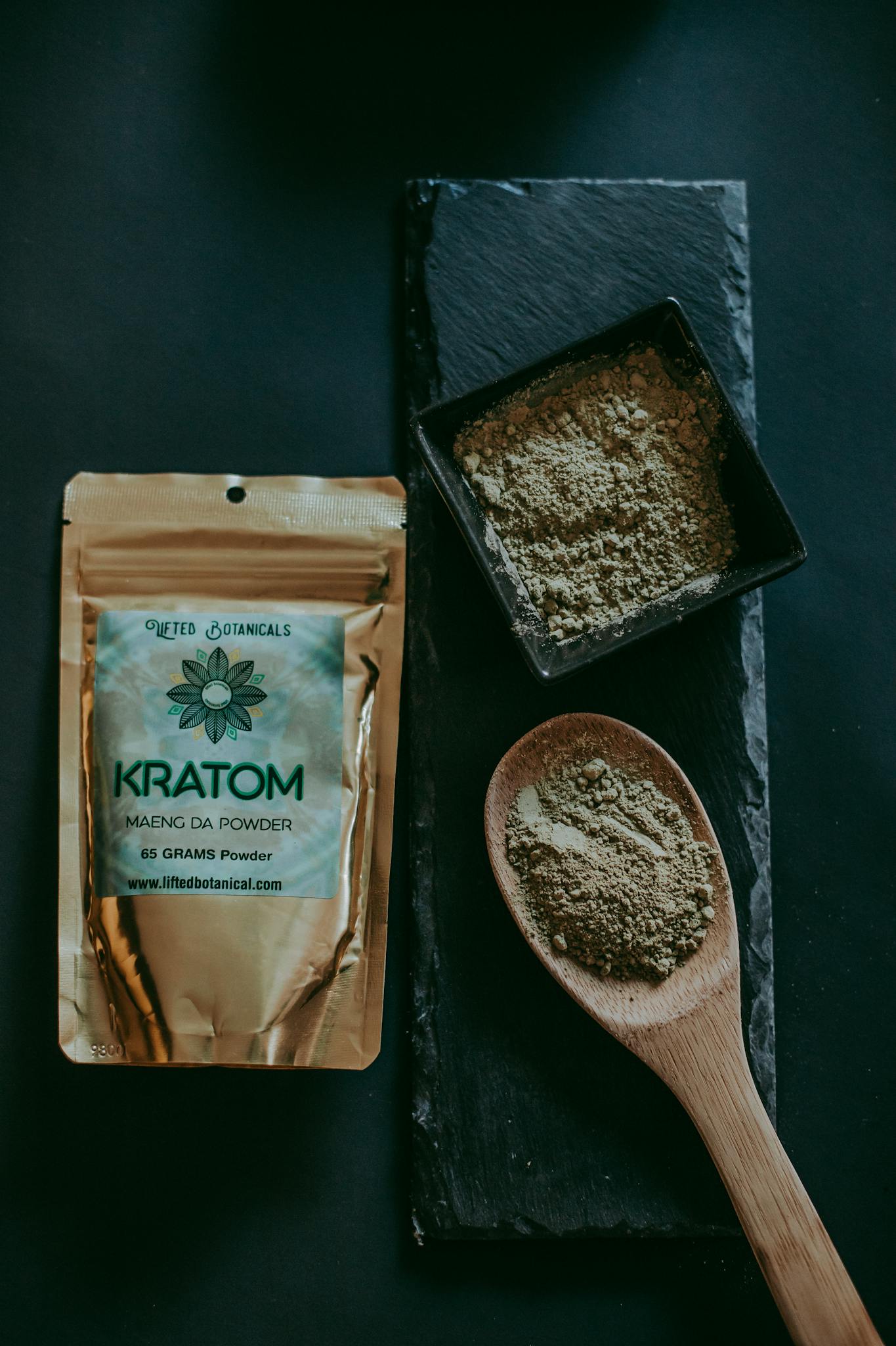 Top view of kratom powder in a bowl and spoon, alongside a branded package, on a dark surface.
